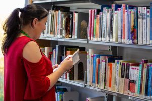 A student stands in front of a row of book shelving, reading a book in their hands